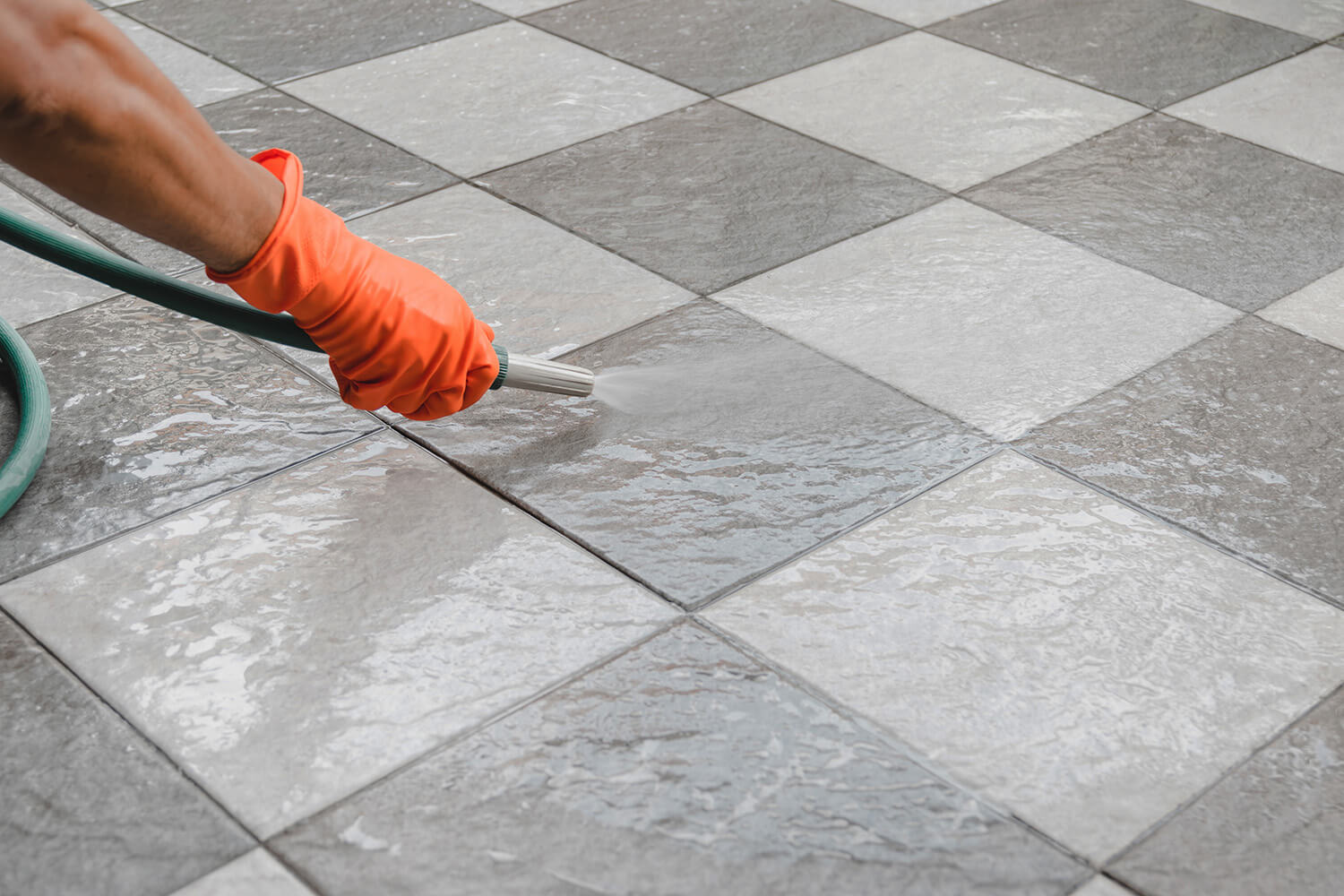 A person wearing orange gloves cleaning tiles and grout